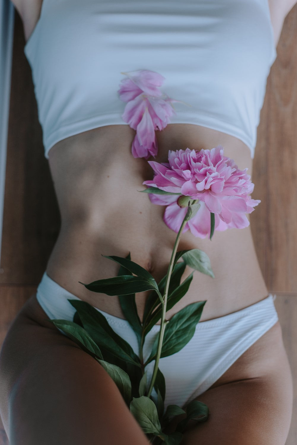 Frau in Unterwäsche mit rosafarbener Blüte auf dem Bauch als Symbol für ein gutes Körpergefühl 