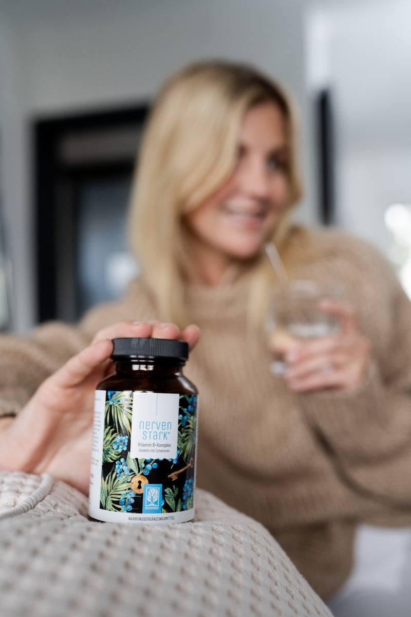 Lächelnde Frau mit einem Glas Wasser und NATURTREU Nervenstark Vitamin B Komplex Kapseln.