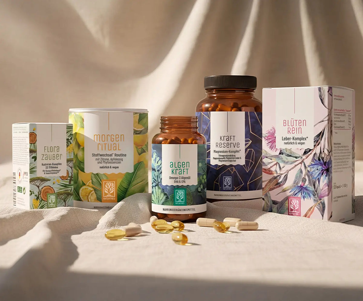 Eine Sammlung von beliebten NATURTREU-Produkten auf einem weißen Tuch in warmen Licht. Produkte von links nach rechts: Florazauber, Morgenritual, Algenkraft, Kraftreserve, Blütenrein.